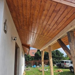 BARWOOD CIESIELSTWO PAWEŁ BARANOWSKI - Drewniana podbitka dachowa z widoczną strukturą drewna, zamontowana na zewnątrz domu z widocznymi elementami konstrukcyjnymi tarasu oraz fragmentem elewacji i otoczenia.