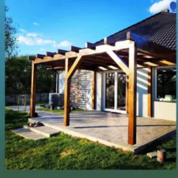 Zadaszenie tarasu z drewnianą konstrukcją, widoczne schodki prowadzące na taras, trawnik i fragment domu z białymi ścianami oraz numer telefonu na dole zdjęcia.