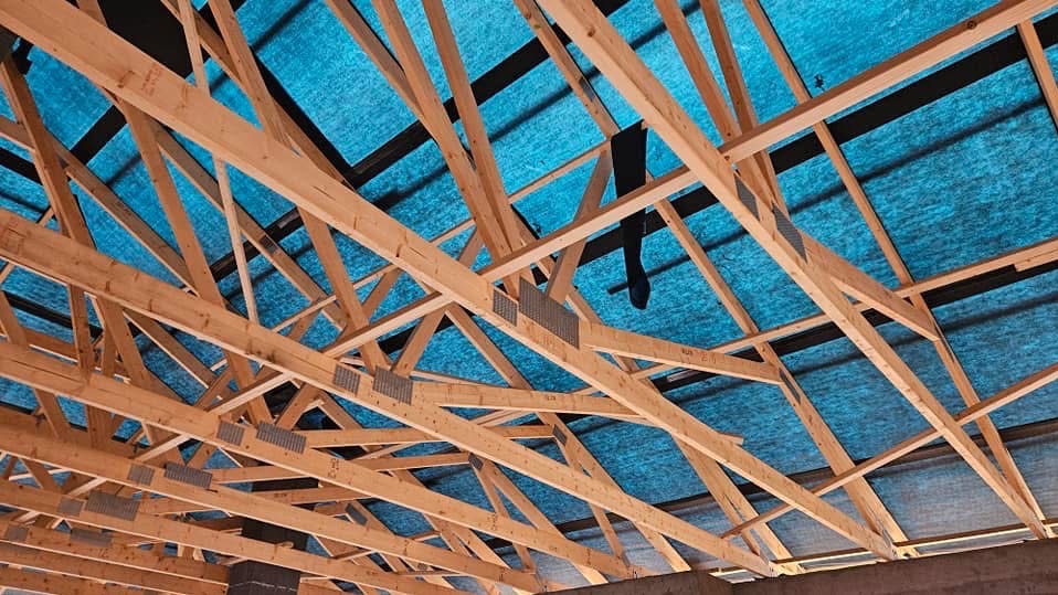 Drewniana więźba dachowa z widoczną membraną w kolorze turkusowym, połączona metalowymi płytkami kolczastymi, widok od dołu.