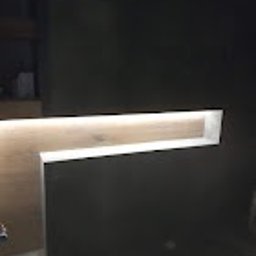 Sunny-home - Niewielka, podświetlana wnęka w ciemnej ścianie, wykończona drewnem o jasnym odcieniu, widoczna z niskiego kąta.