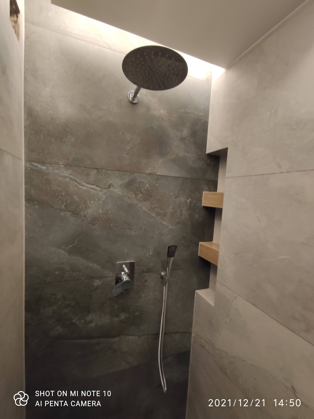 Nowoczesna kabina prysznicowa z szarą, marmurkową okładziną, deszczownicą i półkami wnękowymi z jasnego drewna.