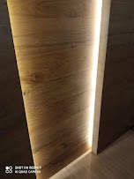 Wąskie ujęcie na fragment ściany z drewnianą okładziną i pionowym paskiem oświetlenia LED wzdłuż krawędzi, widoczny fragment podłogi, ciemne tło.