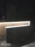 Niewielka, podświetlana wnęka w ciemnej ścianie, wykończona drewnem o jasnym odcieniu, widoczna z niskiego kąta.