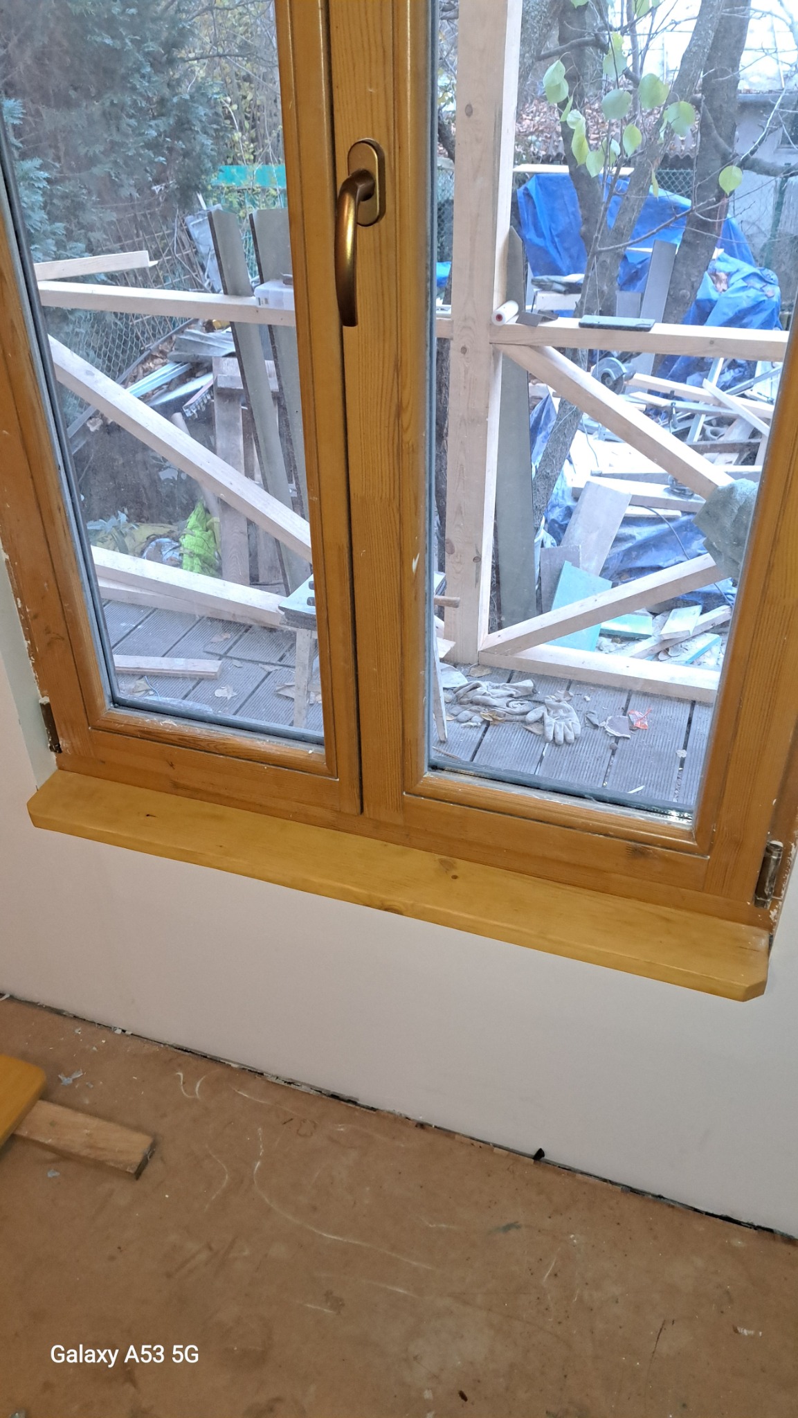 Nowe drewniane okno z widokiem na taras w trakcie budowy, widoczne rękawice robocze i narzędzia na zewnątrz.