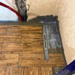 Jakub krasowski - Ułożone drewnopodobne płytki podłogowe w łazience z liniowym odpływem, widoczne krzyżyki dystansowe, instalacja wodna w ścianie i fragment stelaża podtynkowego WC.