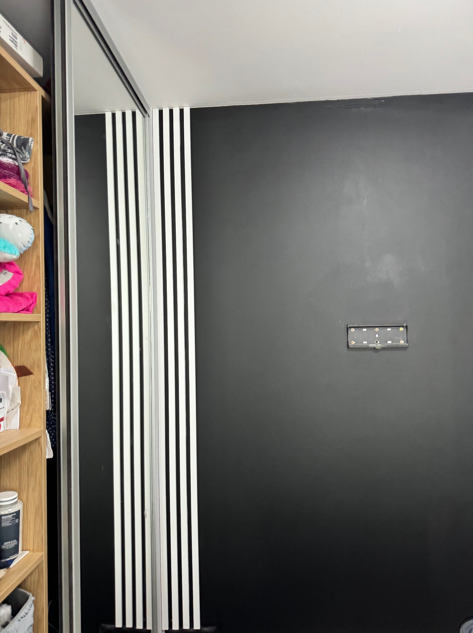 Czarna ściana z zamontowanym uchwytem na telewizor i fragment zabudowy szafy przesuwnej z białymi paskami dekoracyjnymi, widok z mieszkania w Rumi.