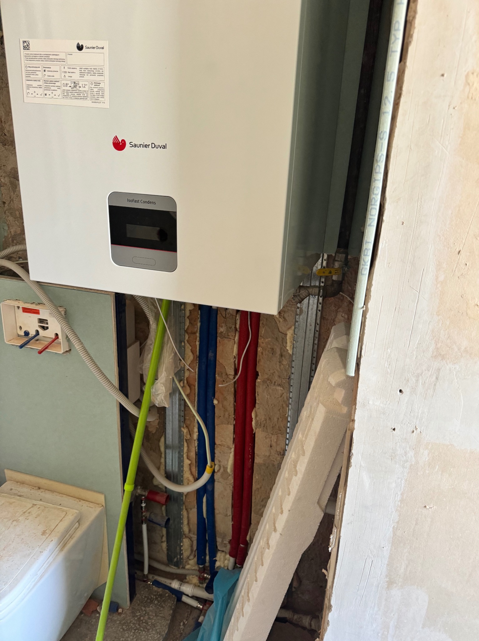 Montaż nowego pieca gazowego Saunier Duval Isofast Condens w trakcie prac remontowych łazienki, widoczne rury instalacji wodnej, profile montażowe i płyty gipsowo-kartonowe.