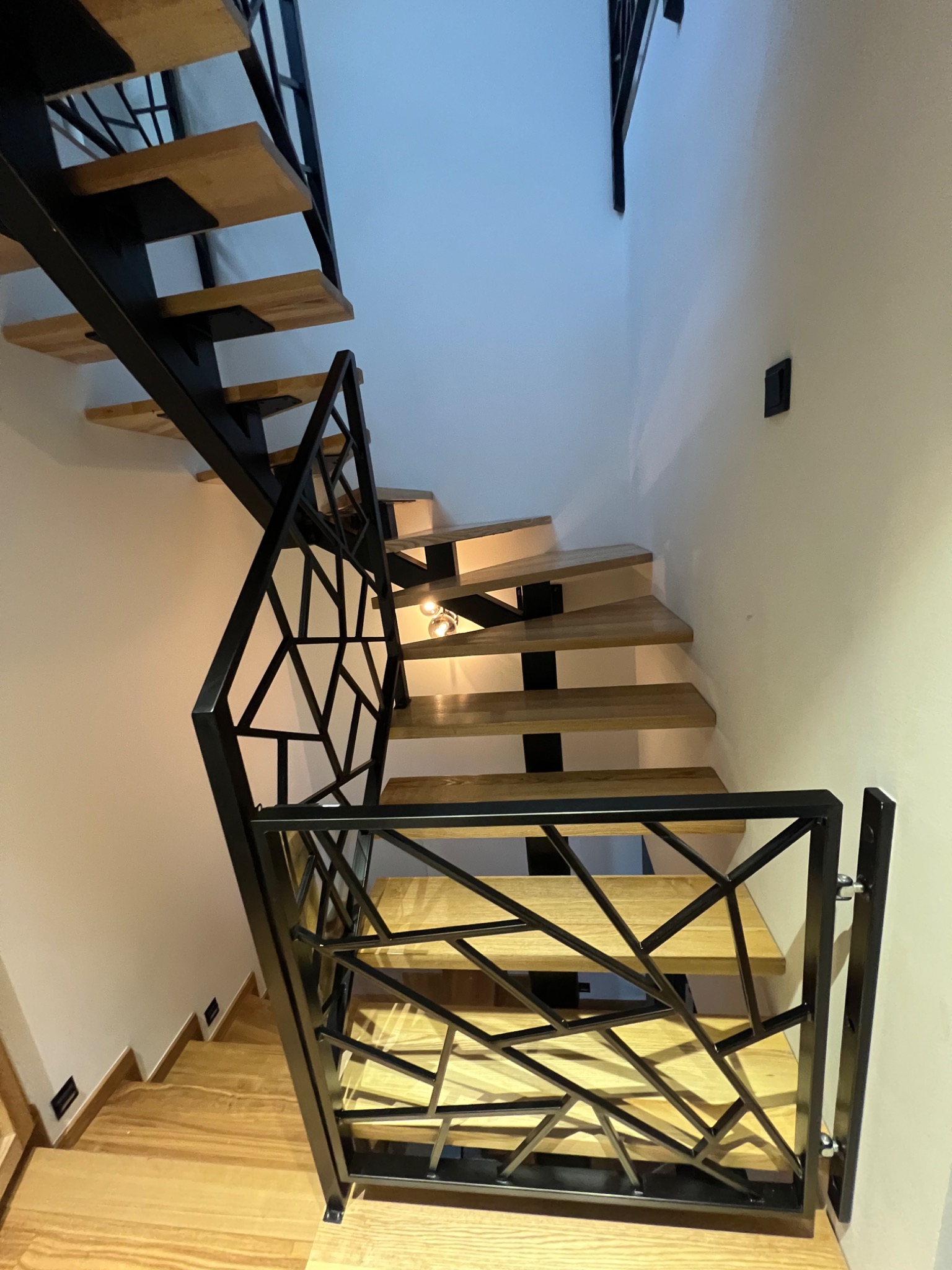 Nowoczesne schody drewniane z czarną, geometryczną konstrukcją. Ujęcie z dołu, podkreślające design i oświetlenie stopni. Minimalistyczne wnętrze.