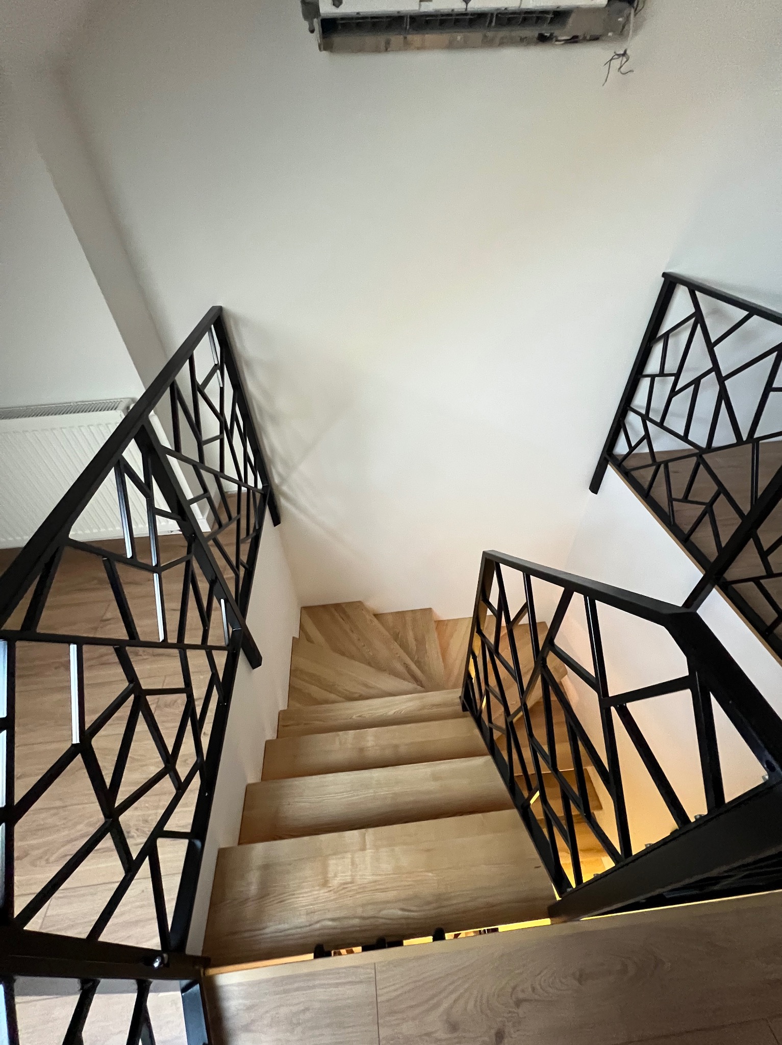 Nowoczesne schody z drewnianymi stopniami i czarną, geometryczną konstrukcją. Ujęcie z góry podkreśla design i jasne wykończenie.