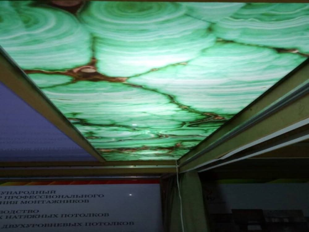 Podświetlany sufit z zielonym wzorem przypominającym malachit, widoczny z perspektywy osoby stojącej pod nim, z fragmentem tekstu w języku rosyjskim na dole.