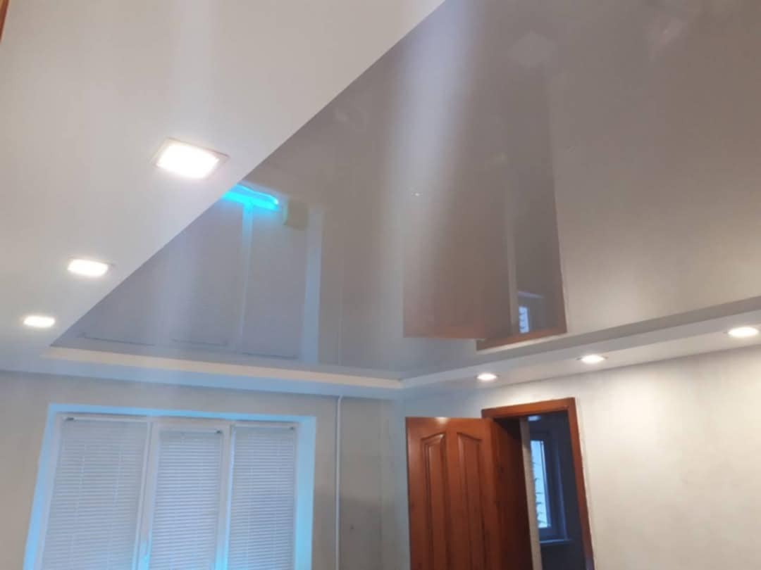 Błyszczący, biały sufit napinany z wbudowanym oświetleniem LED w pomieszczeniu z oknem z żaluzjami i drewnianymi drzwiami.