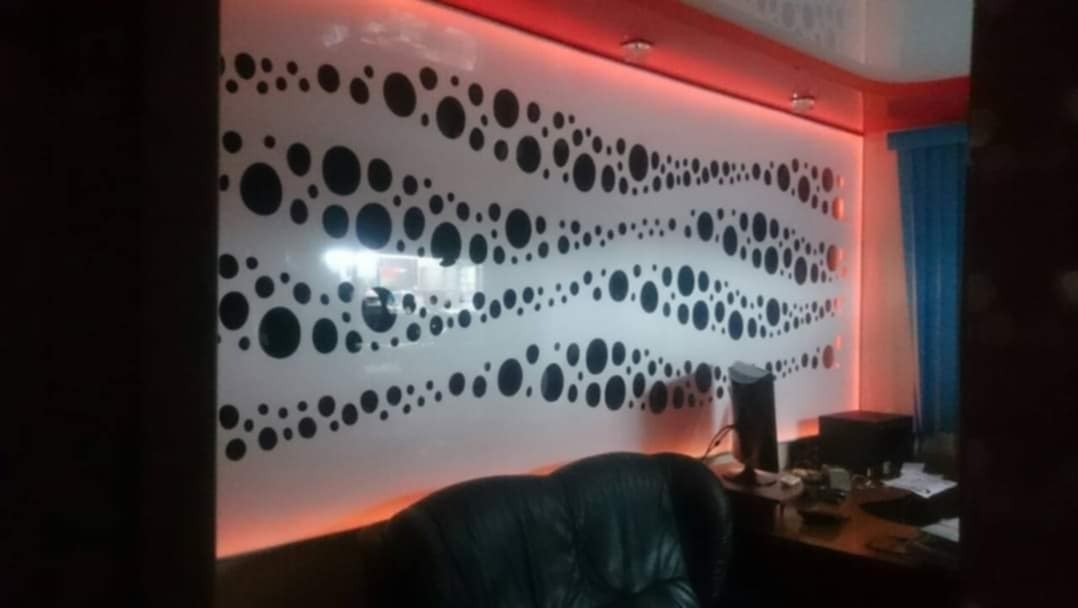 Ściana biura z dekoracyjną folią w czarne kropki, podświetlona czerwonym światłem LED na suficie i podłodze, widoczny fragment biurka z monitorem i dokumentami.