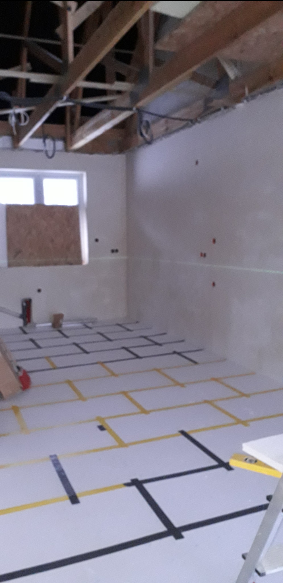Przygotowanie do montażu ogrzewania podłogowego: rozłożona izolacja z taśmami wyznaczającymi układ rur w surowym wnętrzu z drewnianą konstrukcją stropu.