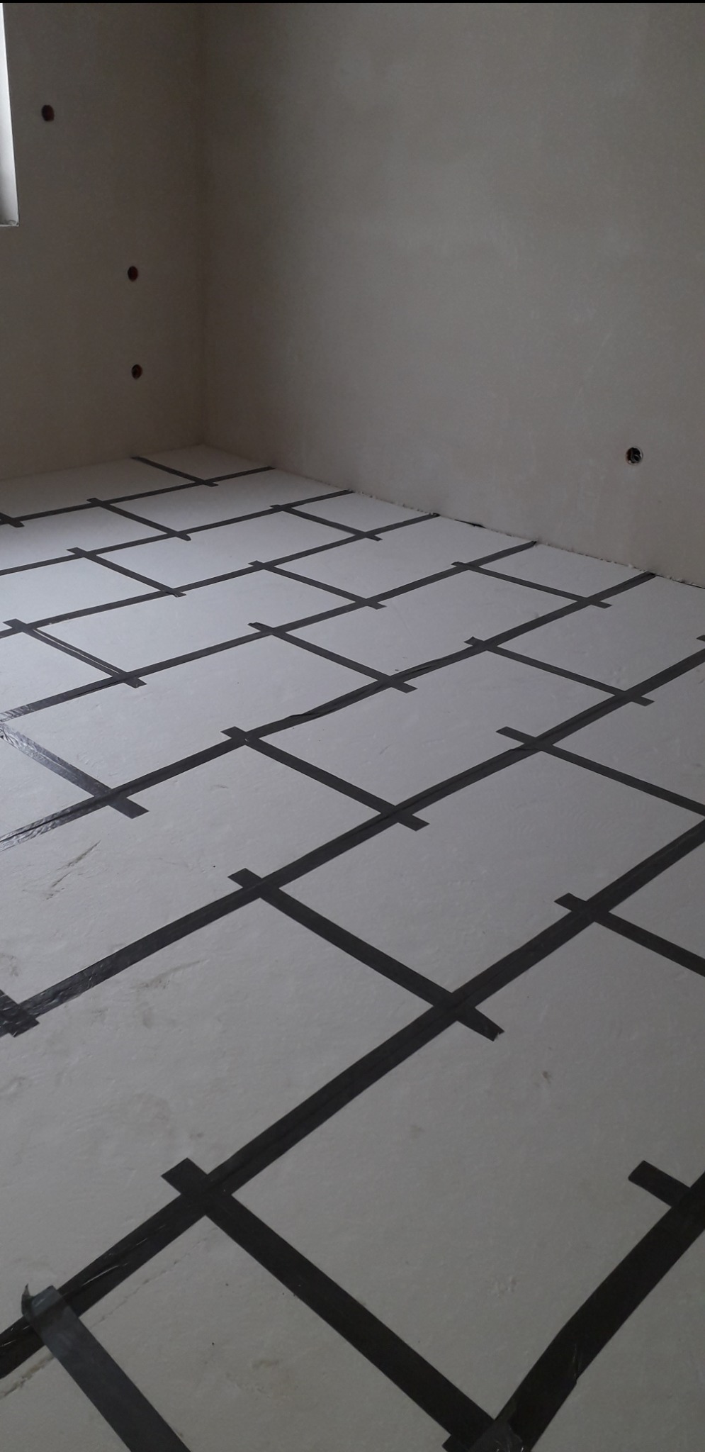 Przygotowanie do ogrzewania podłogowego w Jeleniej Górze: biała mata z czarną taśmą w kratę, widok z góry, surowe ściany z otworami na instalacje.