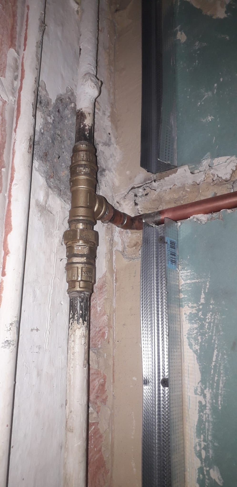 Mosiężny zawór z rurami miedzianymi i stalowym profilem w surowym wnętrzu. Widoczne ślady po instalacji i przygotowania do prac wykończeniowych.