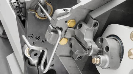 Precyzyjna obróbka metalu na maszynie CNC: detale mechanizmu formującego drut w skomplikowany kształt, widoczne śruby i łożyska.