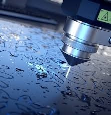 Precyzyjne cięcie laserowe w metalu; widoczna głowica lasera i iskry podczas obróbki, powierzchnia metalu pokryta chłodziwem.