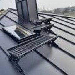 Centrum Dachowe Żyrardów S.C. - Czarny, metalowy dach z zamontowanymi stopniami kominiarskimi i oknem dachowym, widok z góry.