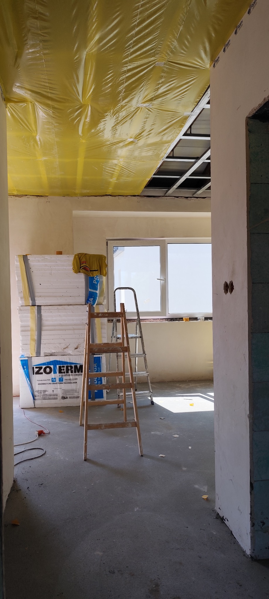 Przygotowanie do montażu sufitu podwieszanego: widoczne profile, folia ochronna, materiały izolacyjne i drabiny w surowym wnętrzu.