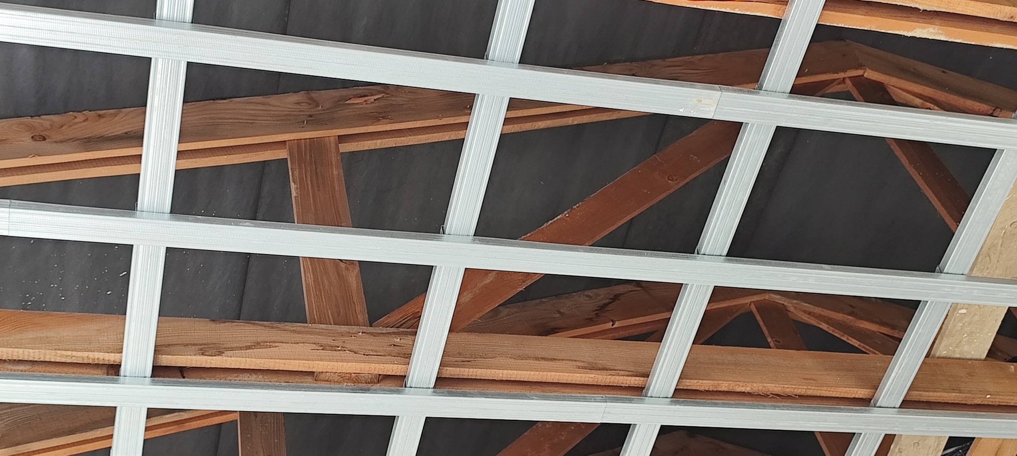 Konstrukcja sufitu podwieszanego z profili stalowych na drewnianej więźbie dachowej, widok z dołu.