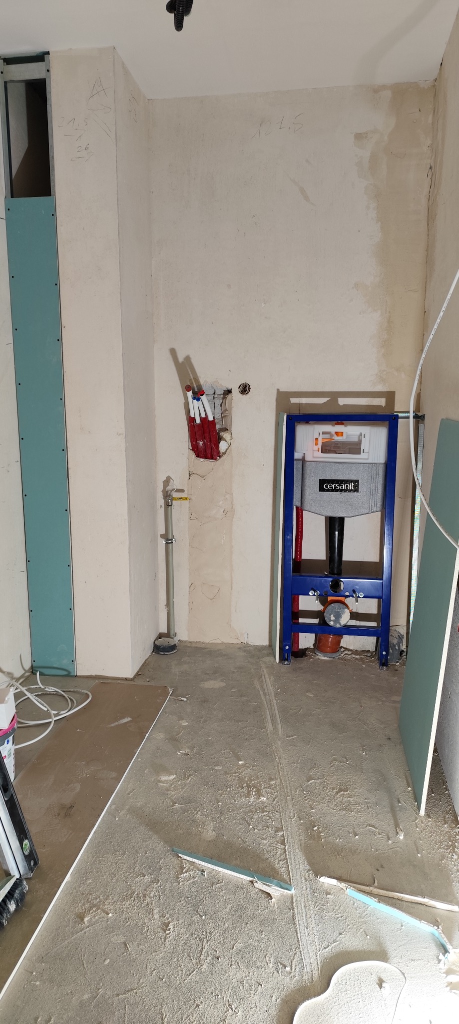 Łazienka w trakcie remontu: widoczne płyty karton-gips na ścianach, stelaż podtynkowy WC marki Cersanit w kolorze niebieskim, rury instalacyjne wystające ze ściany, oraz częściowo ułożona podłoga.