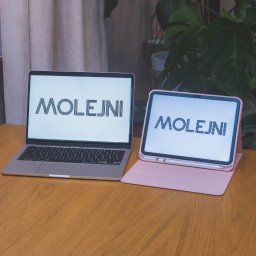 Molejni Marta Jarek - Laptop i tablet obok siebie na drewnianym stole, oba wyświetlają logo 'MOLEJNI', za nimi zasłona i roślina doniczkowa.