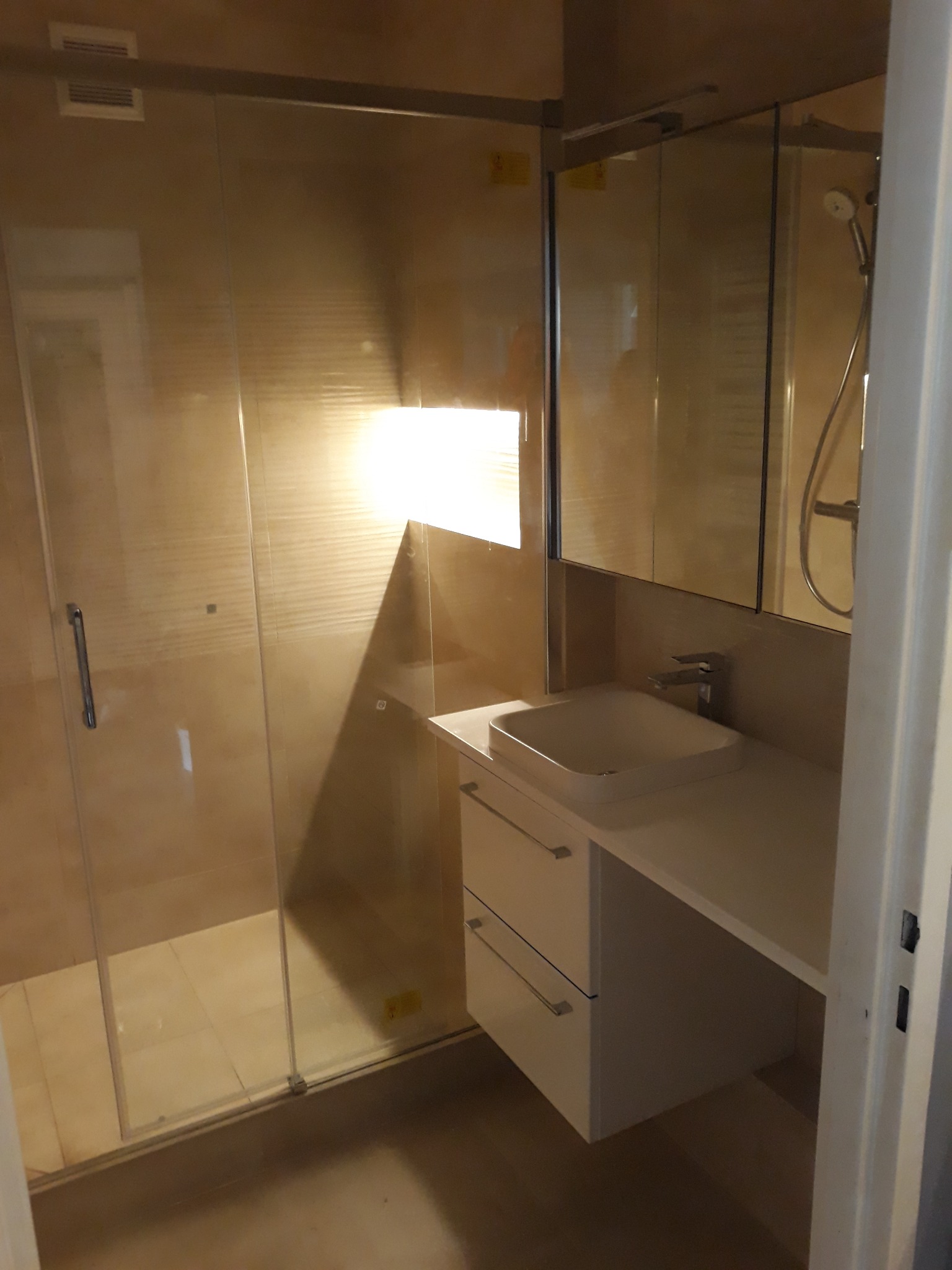 Wykończona łazienka z kabiną prysznicową ze szklanymi drzwiami, umywalką nablatową na szafce z dwiema szufladami i lustrem w zabudowie.