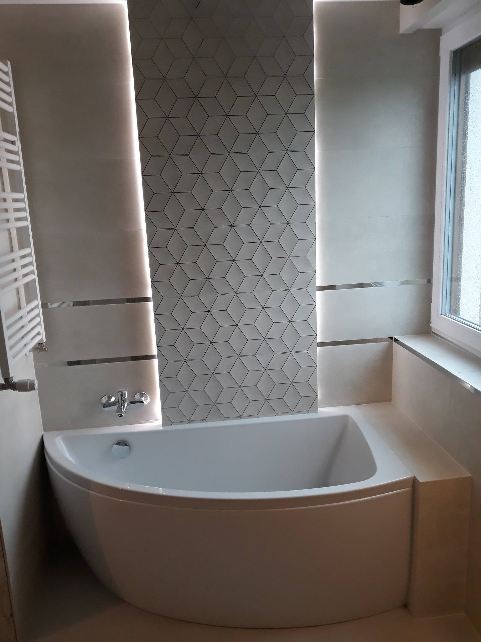 Nowoczesna łazienka z białą wanną narożną, grzejnikiem drabinkowym i geometryczną mozaiką 3D podświetloną LED, wykończona listwami dekoracyjnymi.