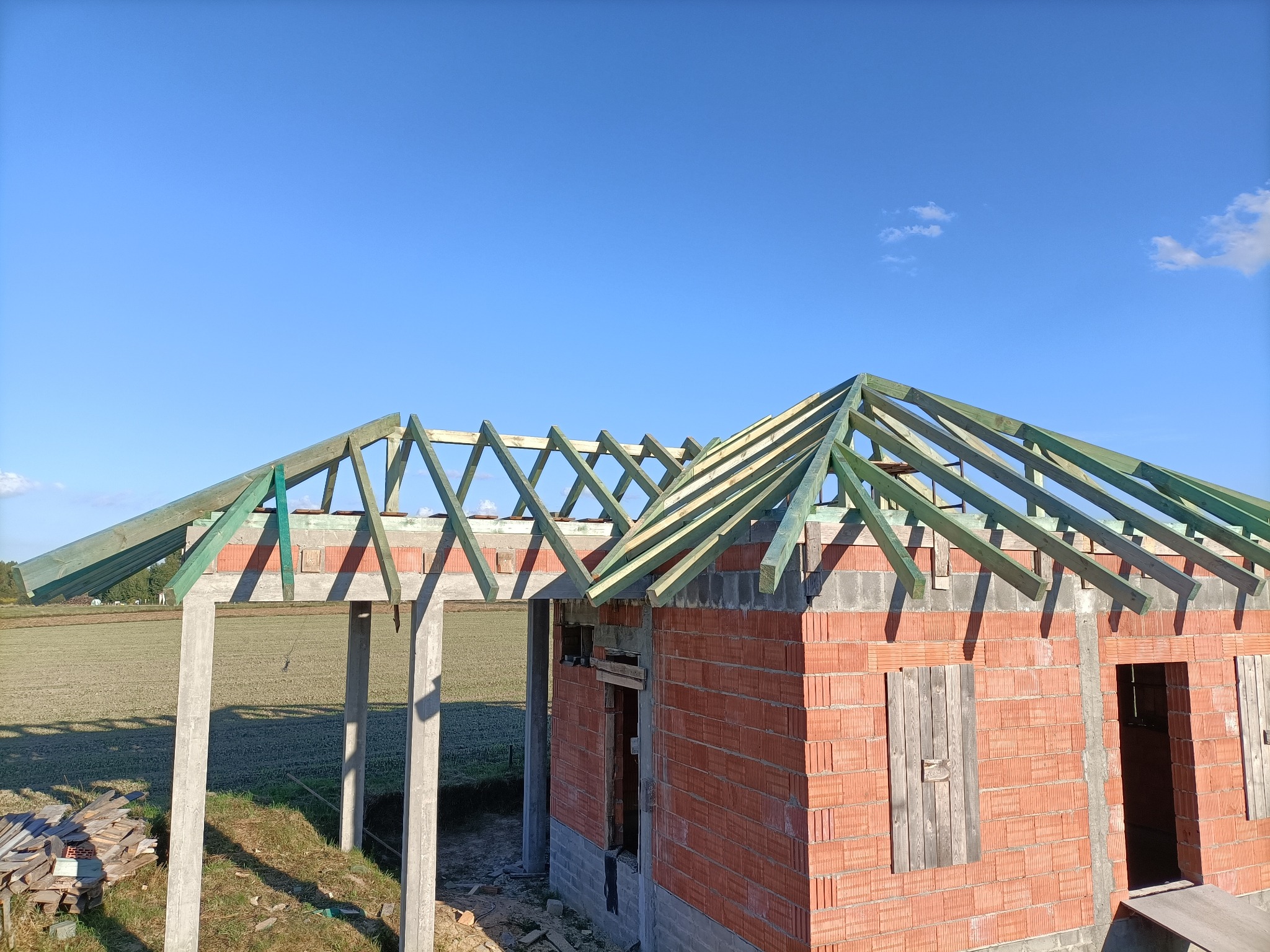 Wznoszenie domu murowanego: konstrukcja dachu z drewnianych belek na tle błękitnego nieba i ceglanej ściany.