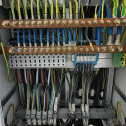 Szafa elektryczna z precyzyjnie ułożonymi kablami o różnych kolorach, podłączonymi do listew zaciskowych i szyn, widok z bliska na instalację elektryczną.