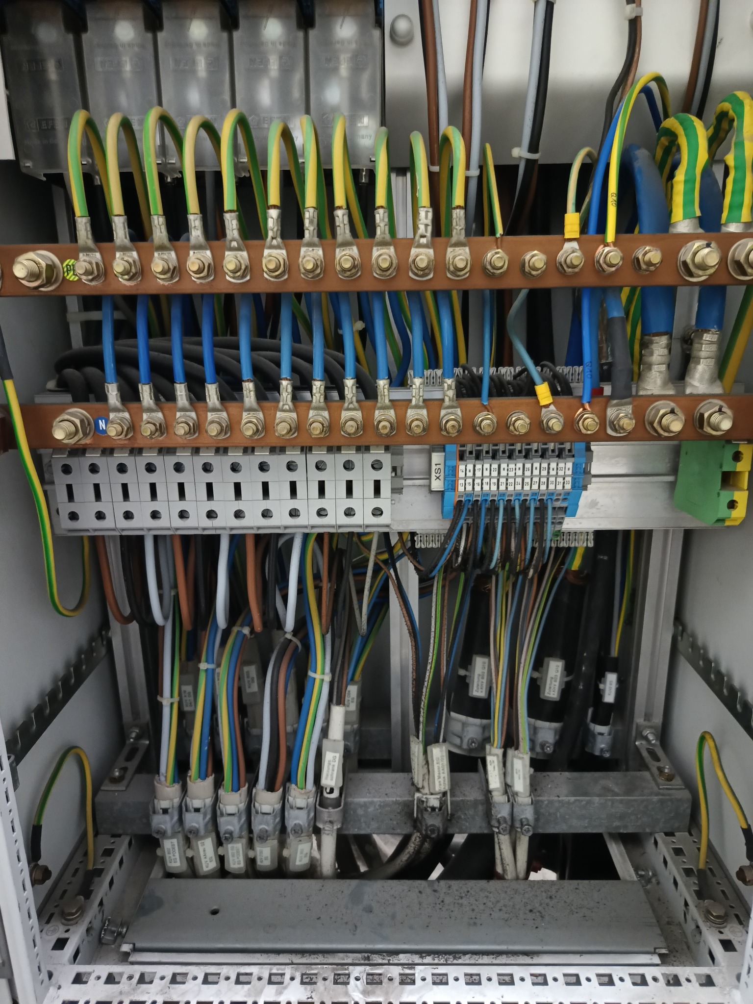 Szafa elektryczna z precyzyjnie ułożonymi kablami o różnych kolorach, podłączonymi do listew zaciskowych i szyn, widok z bliska na instalację elektryczną.