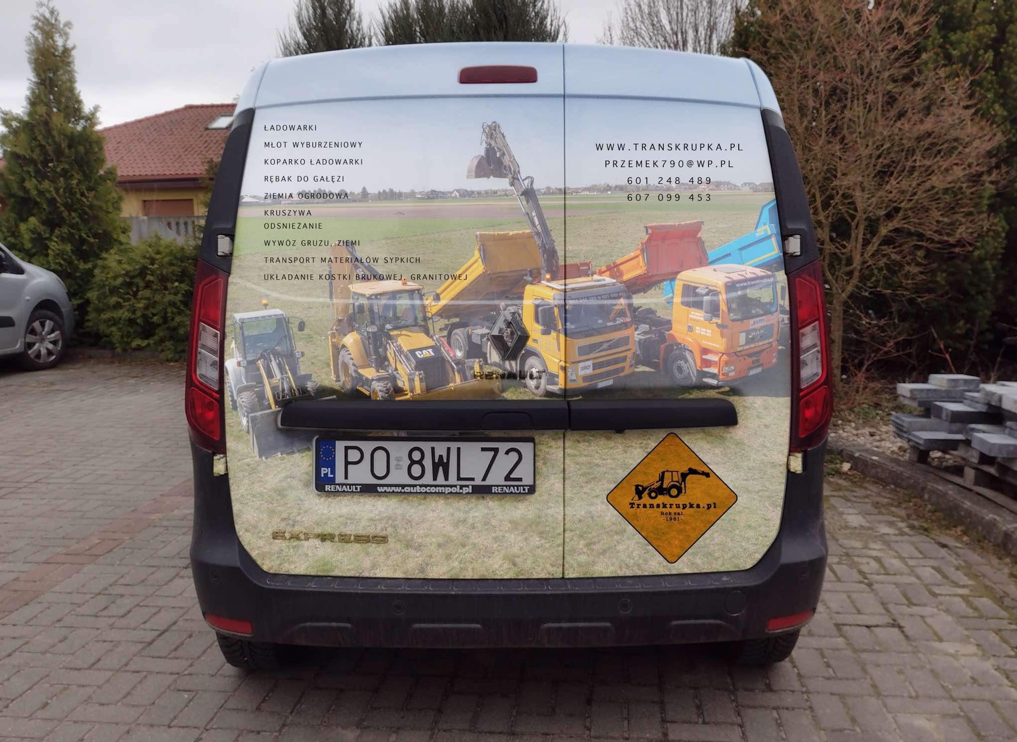Tył samochodu dostawczego Renault Express z oklejeniem reklamowym firmy budowlanej Transkrupka. Na okleinie widoczne grafiki przedstawiające maszyny budowlane: koparki, ładowarki i wywrotki na tle...
