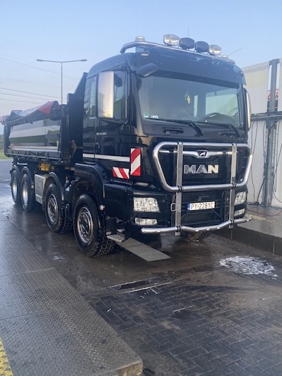 Czarny, umyty samochód ciężarowy MAN z odkrytą skrzynią ładunkową, zaparkowany na platformie myjni z widoczną tablicą rejestracyjną PY 2281C.