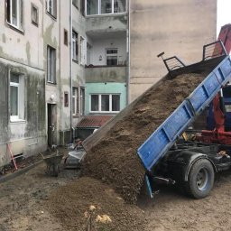 Misza-Bud usługi zimne minikoparką - Ciężarówka z wywrotką wysypuje ziemię na dziedzińcu kamienicy, widoczne narzędzia i elementy przygotowania terenu.