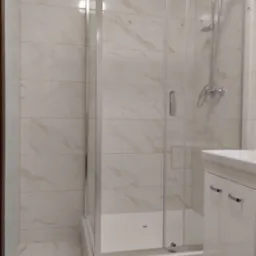 Nowoczesna kabina prysznicowa z przezroczystego szkła i chromowanymi detalami, zamontowana w łazience wykończonej płytkami imitującymi marmur, obok biała szafka pod umywalkę z chromowanymi uchwytami.