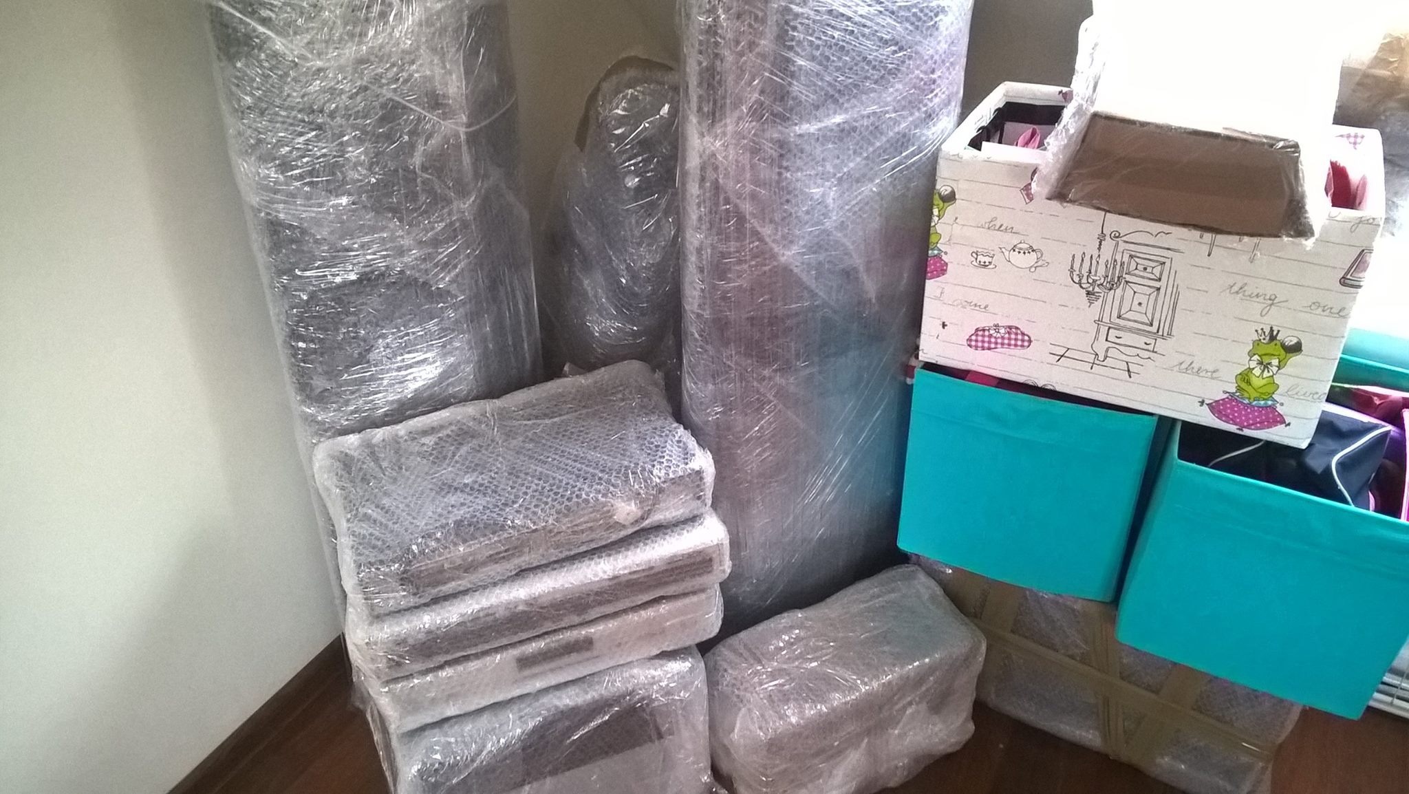 Spakowane przedmioty, w tym zwinięte dywany i kartony, owinięte folią stretch, przygotowane do transportu.