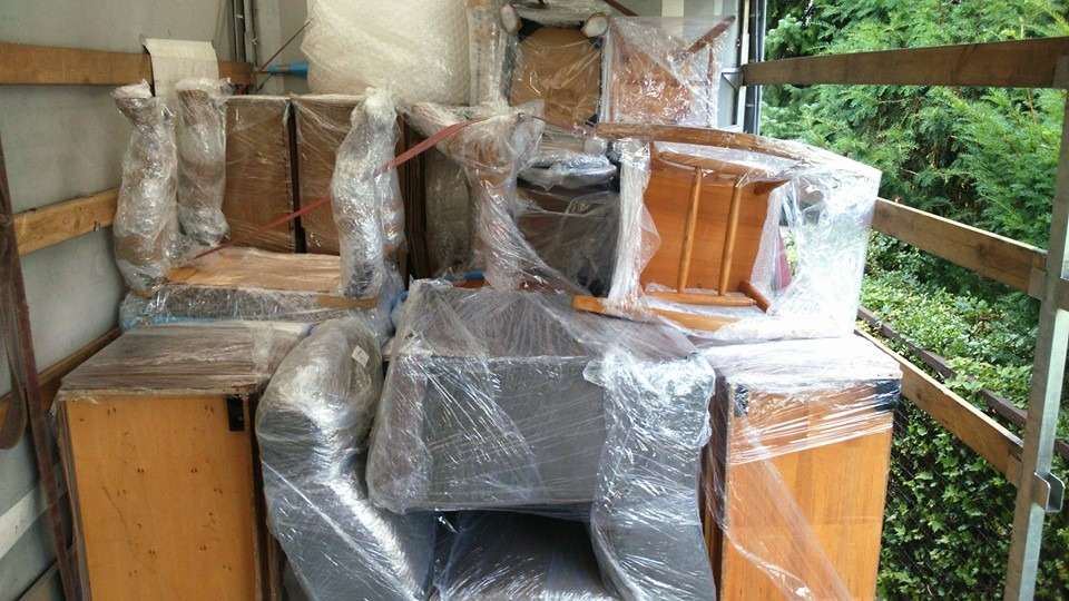 Meble zabezpieczone folią stretch wewnątrz skrzyni ładunkowej samochodu dostawczego, widoczne krzesła i szafki w trakcie transportu.