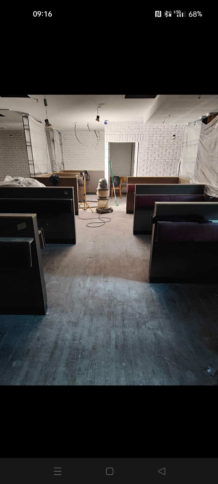 Wnętrze lokalu w trakcie remontu, z widoczną maszyną do obróbki podłóg i częściowo osłoniętymi meblami, parkiet po obróbce, biała cegła na ścianach.
