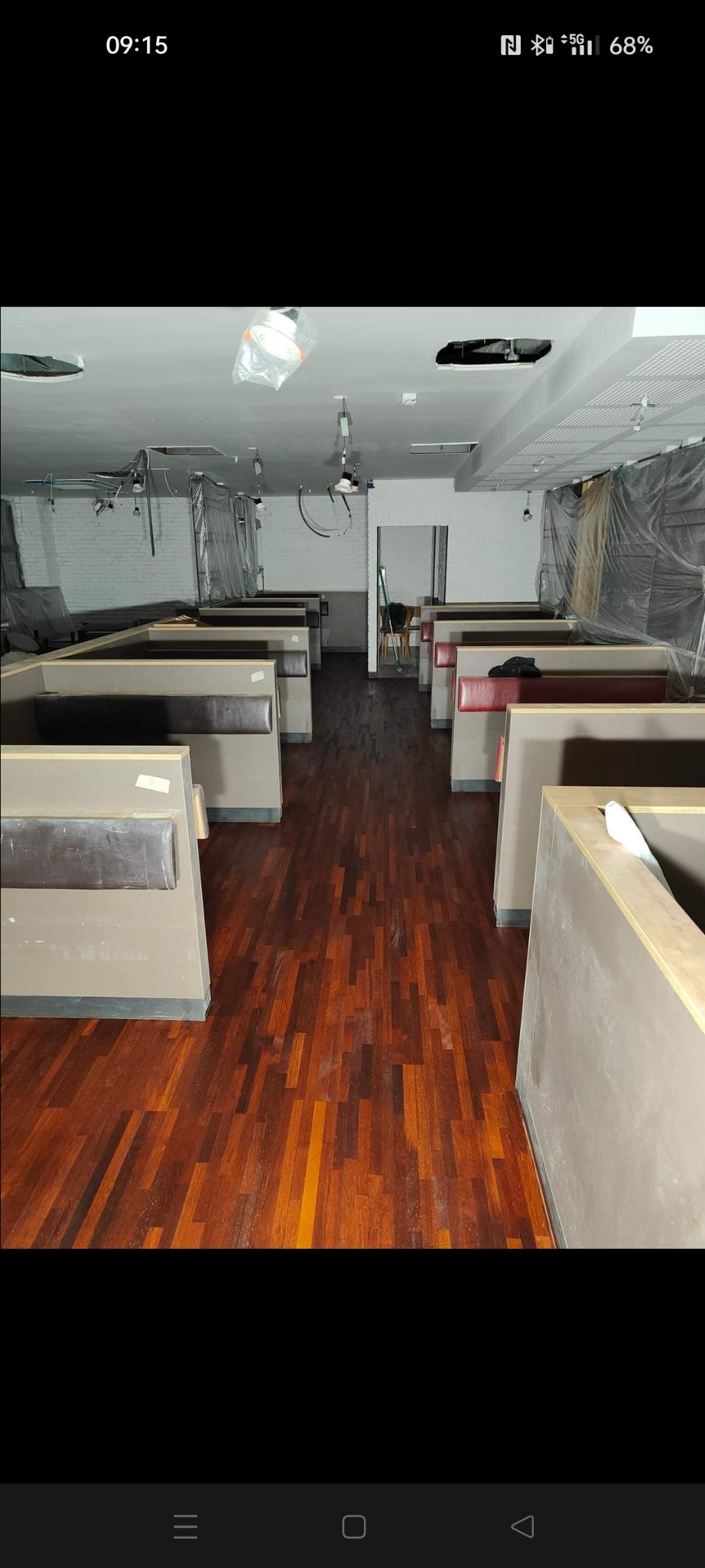 Wnętrze lokalu w trakcie remontu, widoczna świeżo położona, lakierowana podłoga parkietowa z ciemnego drewna, kabiny z obiciami w tle, ściany częściowo zabezpieczone folią malarską.