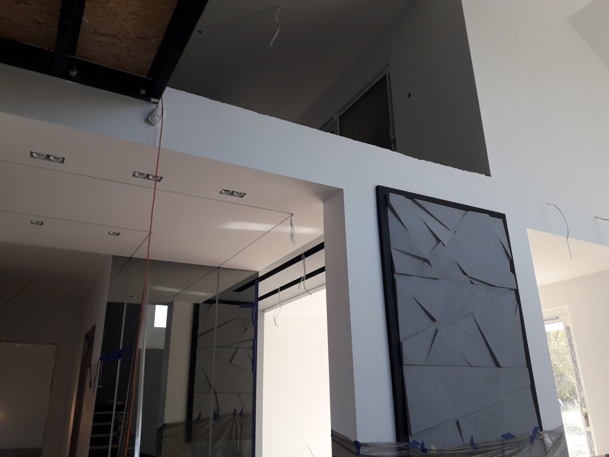 Wnętrze w trakcie remontu: ściany przygotowane do malowania, zabezpieczone folią, widoczna płyta dekoracyjna z geometrycznym wzorem i instalacja elektryczna.