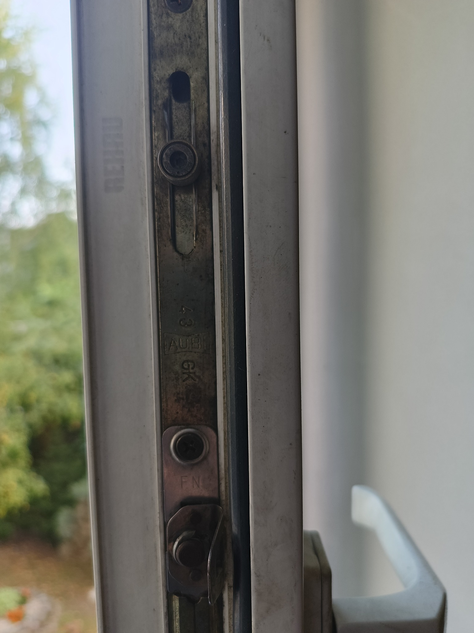 Detal okna PCV marki REHAU z widocznym mechanizmem blokującym AUBI 43 GK i FN, wymagającym potencjalnej regulacji lub konserwacji.
