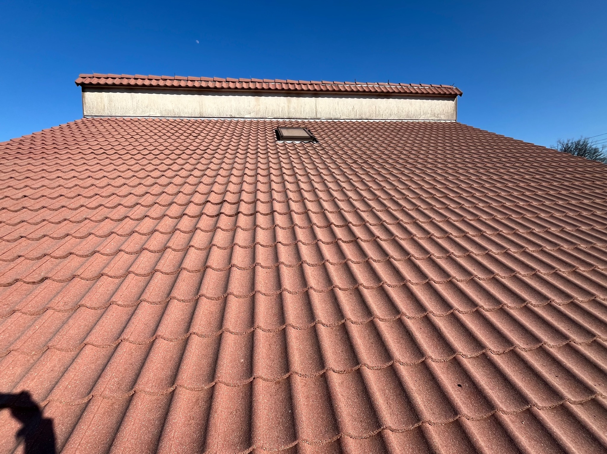 Czerwona dachówka ceramiczna na skośnym dachu z oknem dachowym, widok z dołu w słoneczny dzień.