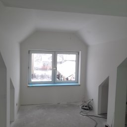 Darson Remonty Dariusz Kukulski - Poddasze po remoncie, świeżo pomalowane na biało, z oknem zabezpieczonym folią malarską, widoczne przewody elektryczne na podłodze.