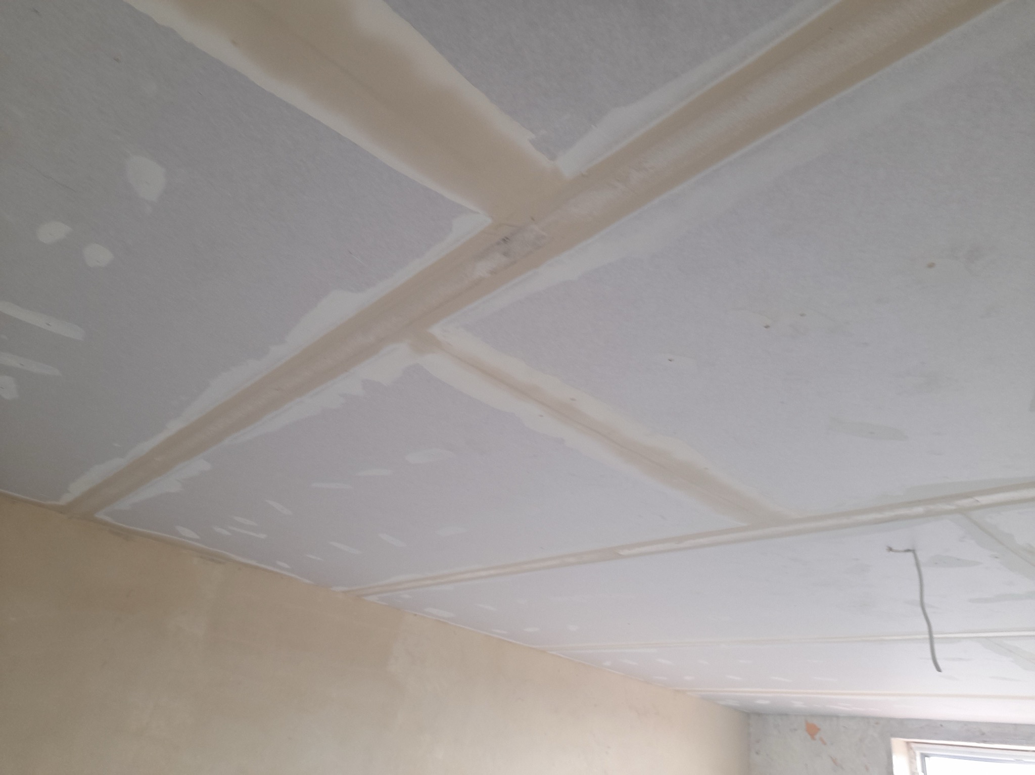 Sufit z płyt karton gipsowych, z widocznymi łączeniami zaszpachlowanymi i przygotowanymi do dalszej obróbki, fragment ściany w kolorze beżowym.