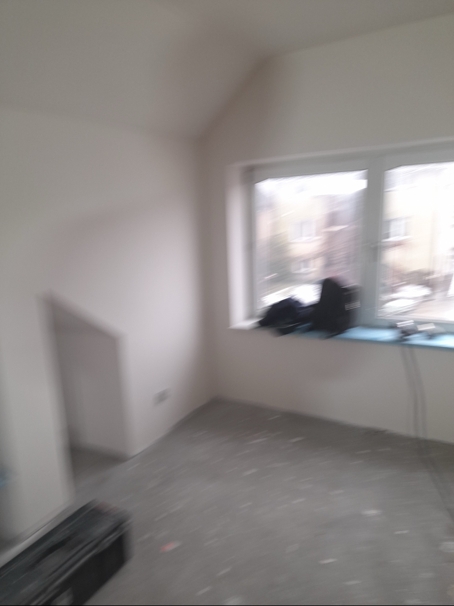 Pokój w trakcie remontu, ściany przygotowane do malowania, widoczne ślady szpachlowania na podłodze, narzędzia i torba robocza na parapecie okiennym.