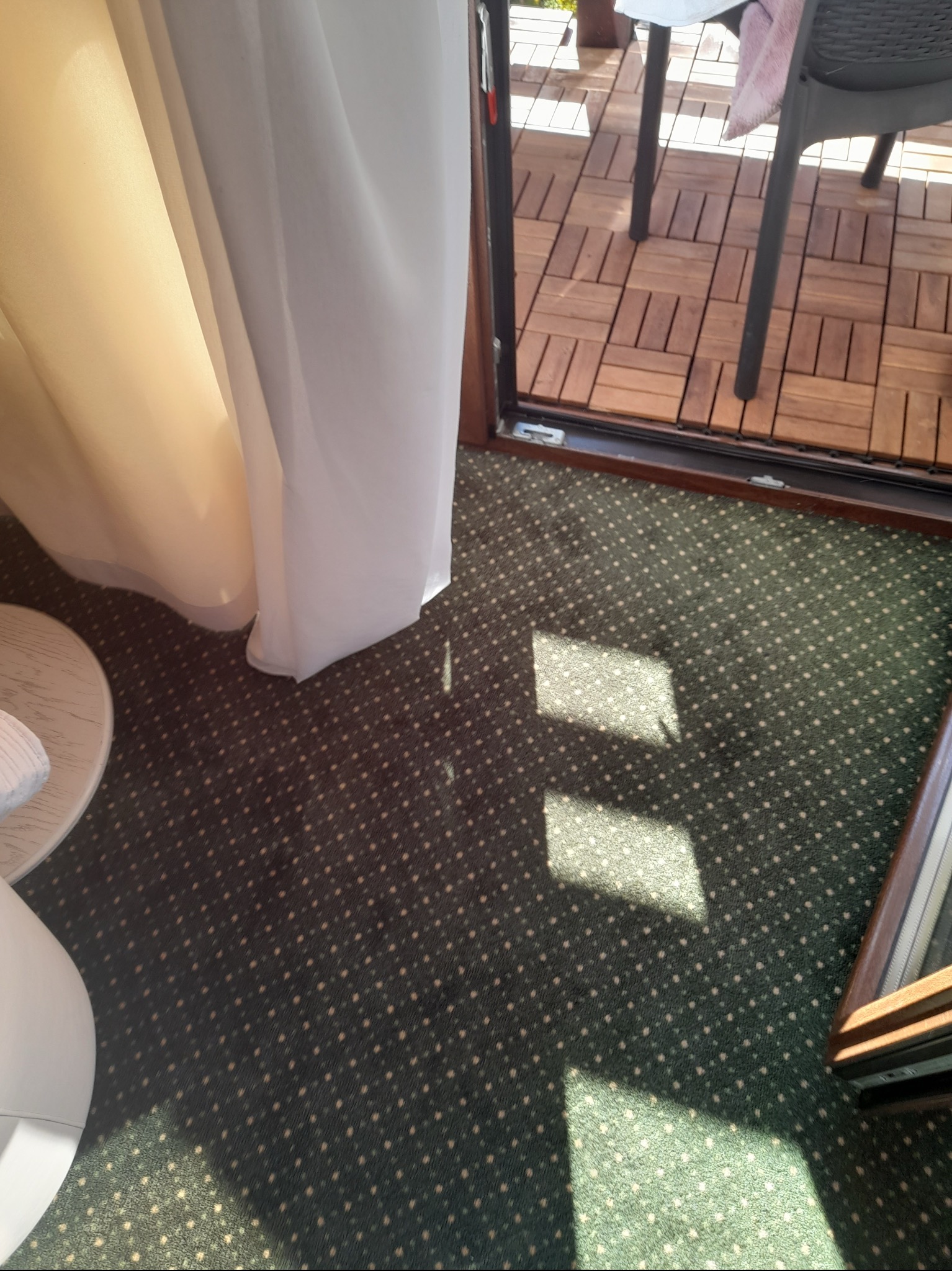 Fragment pokoju z zasłoną, dywanem w kropki i wyjściem na balkon z drewnianą podłogą