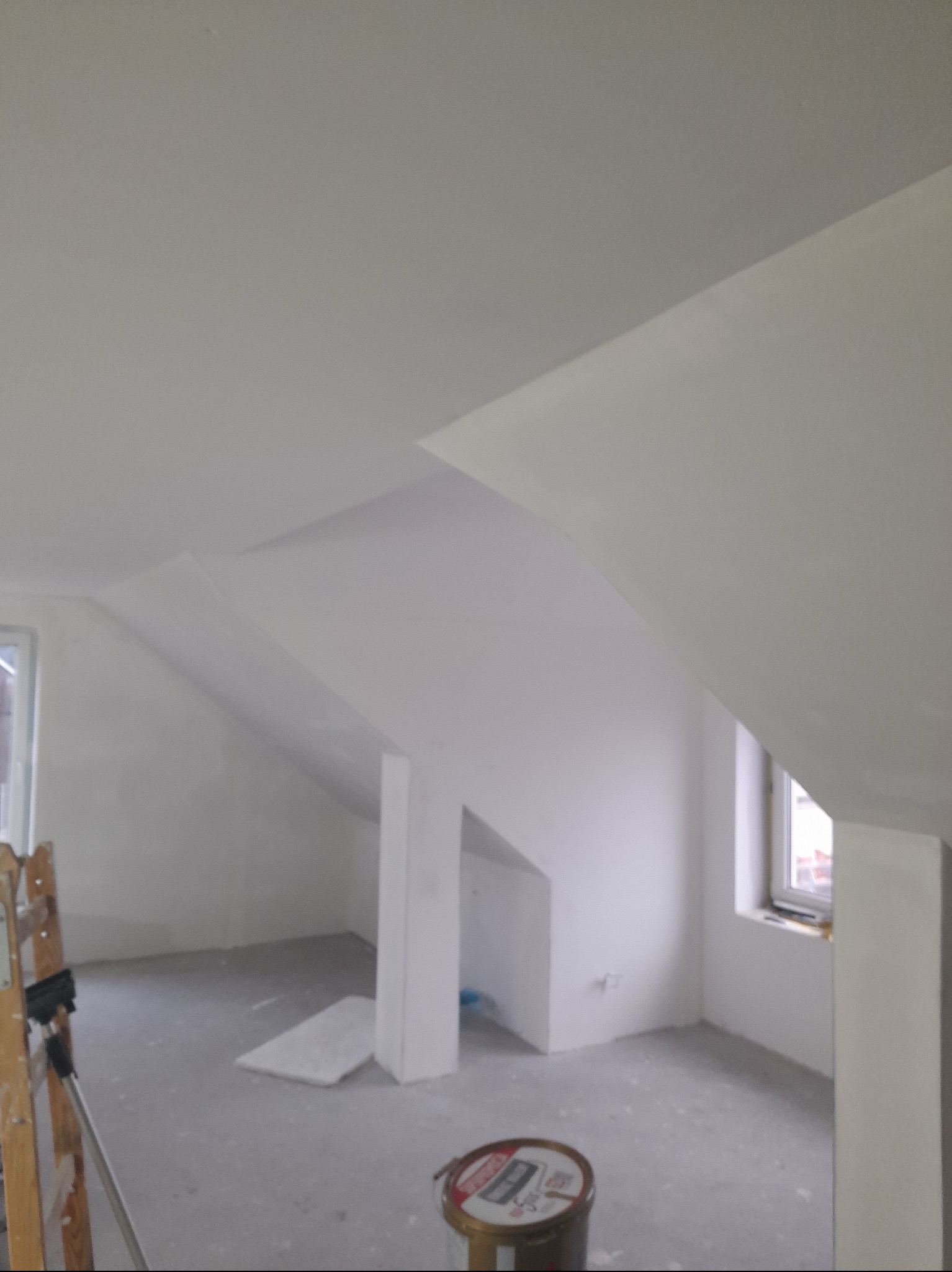 Poddasze po pracach wykończeniowych, widoczna skośna ściana, pomalowane na biało, drabina malarska i puszka farby na podłodze.