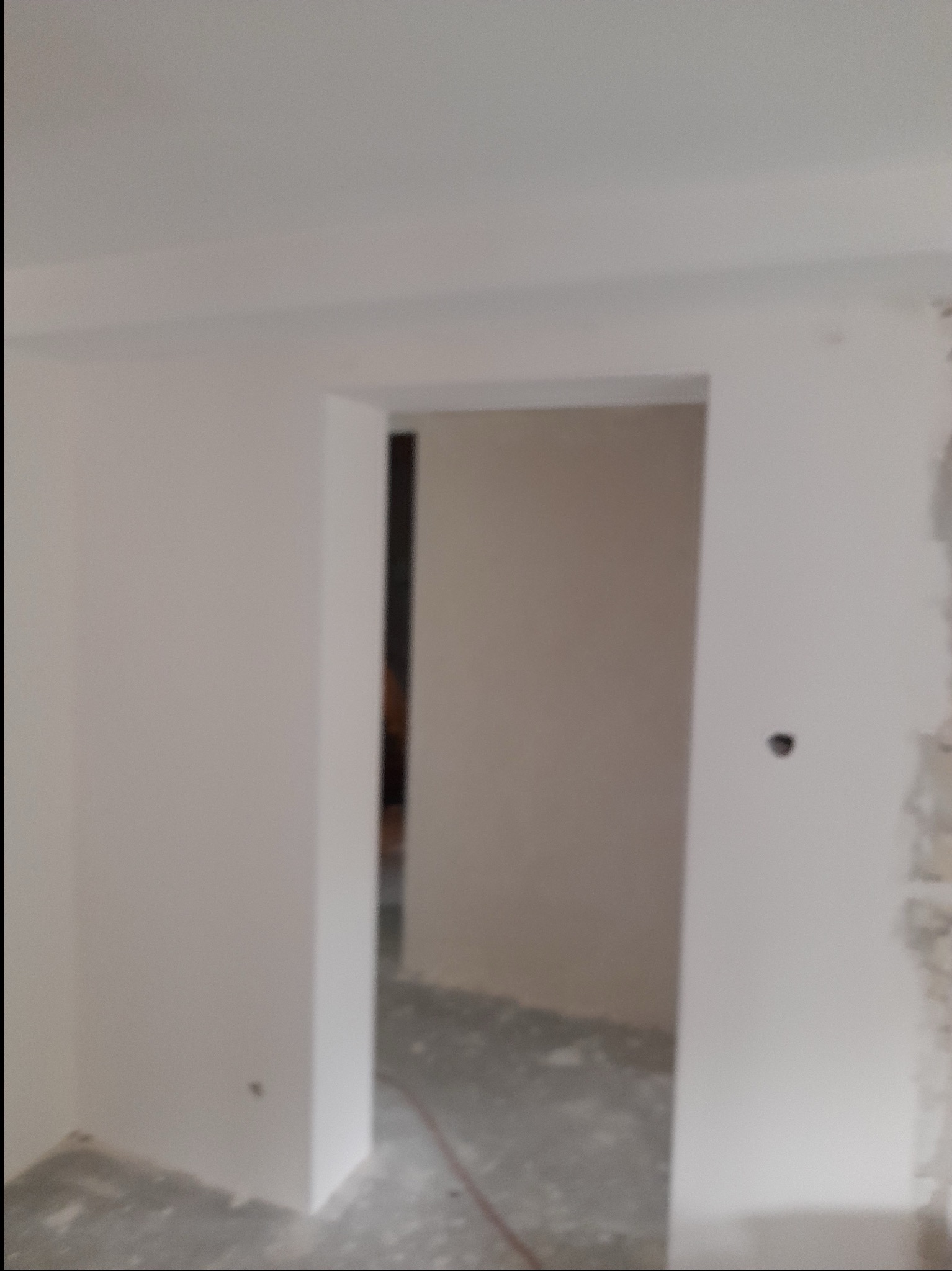 Świeżo wyszpachlowane ściany i futryna drzwiowa w trakcie remontu, widoczne niedoskonałości na ścianie po prawej stronie.