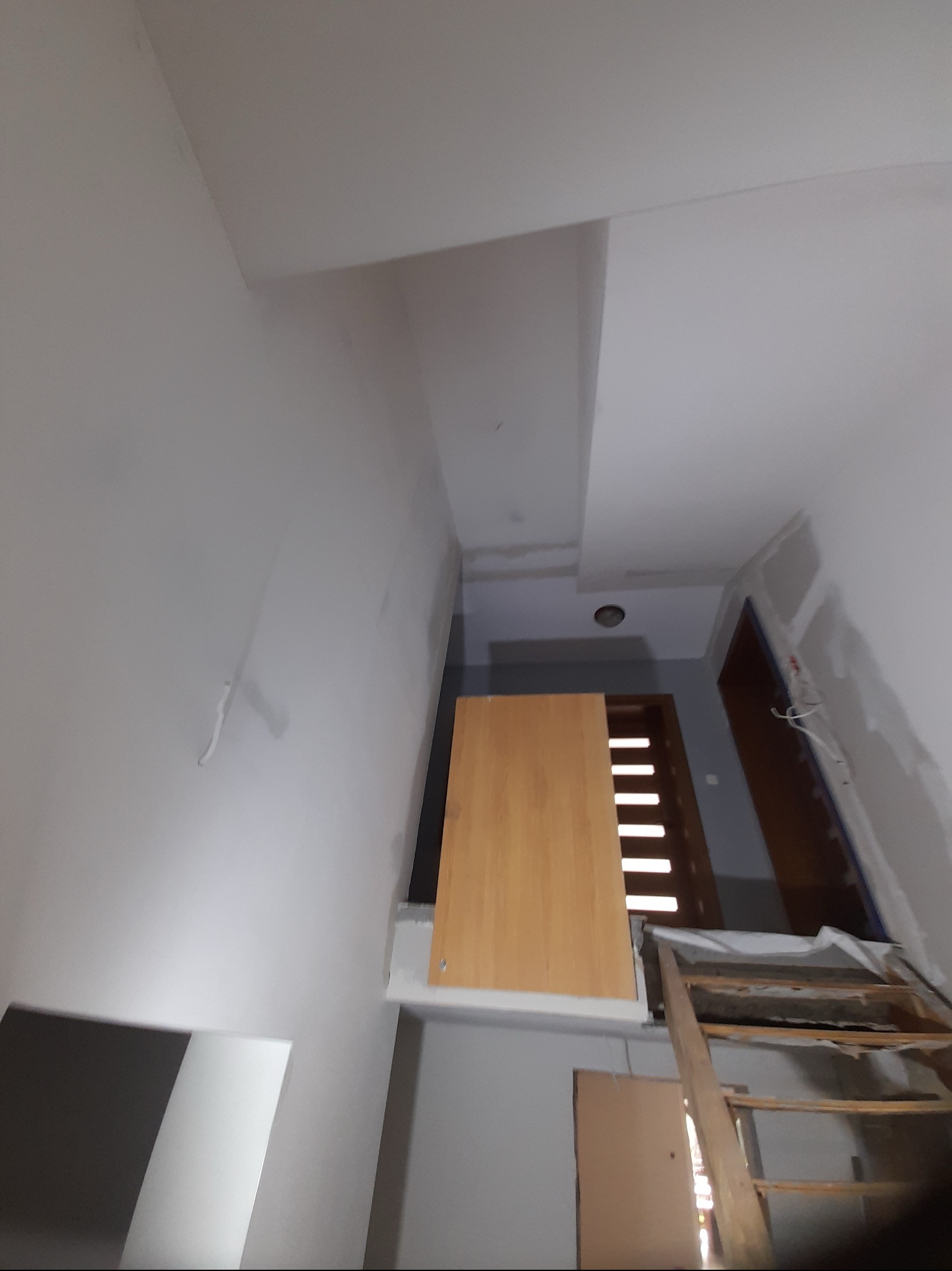 Wnętrze w trakcie prac wykończeniowych, widoczne ściany przygotowane do malowania, fragment płyty karton gips na suficie, drewniane schody malarskie i zabezpieczone folią drzwi wejściowe.