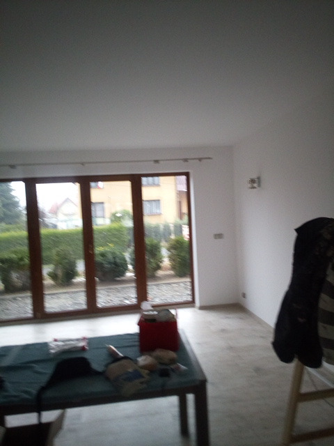 Pokój po malowaniu ścian na biało, widoczne narzędzia malarskie na stole, okno z widokiem na ogród.